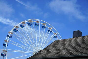 Riesenrad hinter altem grauem Hausdach bei Sonne am Mittag im Sommer
