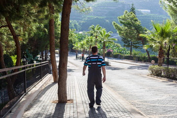 A working man walks along road among trees, view from back.