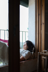 girl on balcony reading relaxed, woman in her twenties in rural house relaxing with a book, coffee with milk on a stool, brunette with skin and face dressed in a jumpsuit.