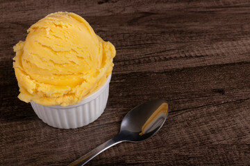 Tasty yellow ice cream served in a white bowl next to a spoon. Gastronomic photography ice cream parlors and gelateries . Image with empty space on the right.
