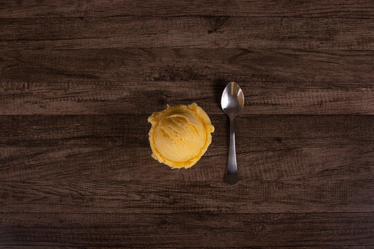 Yellow cream ice cream served in a white porcelain pot next to a spoon. Top view photography.