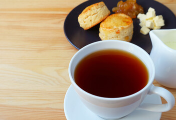 Closeup a cup of hot tea with a plate of scones in the backdrop
