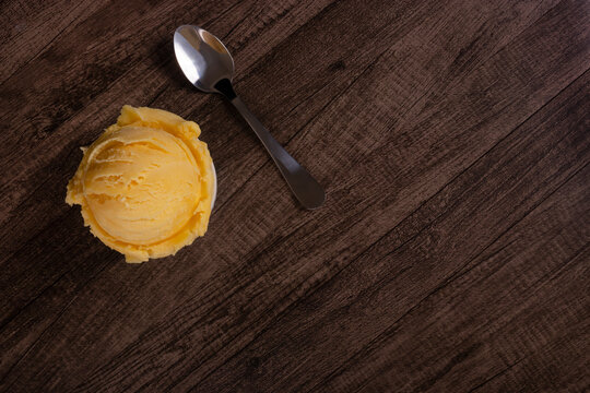 Tasty yellow cream ice cream served in a white bowl next to a spoon. Top photo with elements in the upper left corner of the image and empty space on the right. Ice cream ball.