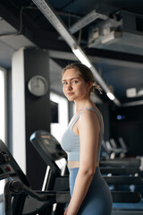 young girl in a tracksuit training on a treadmill in the gym