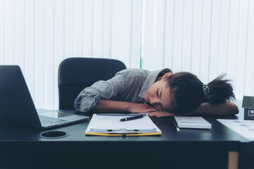 Exhausted and tired young adult office worker falling asleep on desk because of overtime work hours. Burnout fatigued company employee being sleepy and stressed because of huge work effort.