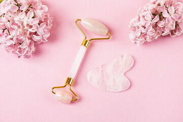Pink jade roller and gua sha for face massage with flowers daffodils and lilacs. Facial massager...