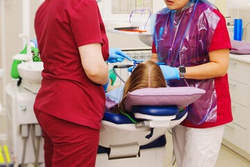 A pediatric dentist treats or performs oral hygiene for a little girl.