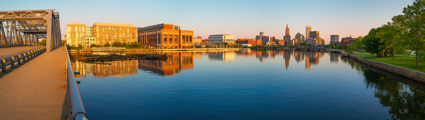 Fototapeta na wymiar Panoramic metropolitan cityscape at sunrise, skyline and industrial buildings, tranquil water reflections, and the old Point Street Bridge over Providence River in Rhode Island 