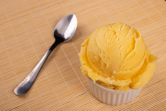 Yellow colored cream ice cream served in a white pot with spoon on the side and wooden background . Gourmet photography close-up ice cream and gelateria products.