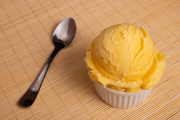Yellow ice cream served in a white pot. Tasty traditional yellow gelato enjoyed around the world. Spoon tilted diagonally next to food. Close-up photography .