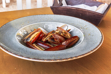 Cooked Lithofaga date shell mussels served on a dish at a wooden table.