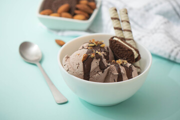 Chocolate ice cream decorated with nuts and chocolate icing, in a white bowl, blue background. Summer homemade cooling desserts