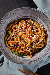 A vertical top view of a luscious bowl of Udon noodles mixed with chicken and vegetables. The...