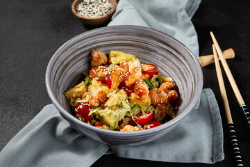 Side view of an Asian salad with shrimps and pineapples in a bowl on a black background, with a textile napkin beside the bowl.