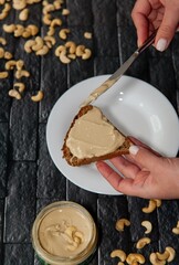 female hands spread nut butter with a knife on bread