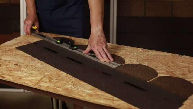 The process of cutting bituminous roofing tiles by a master indoors close-up