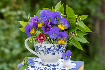 Blumenstrauß mit blauen Hornveilchen und Storchschnabel in einer Tasse mit floralem Motiv