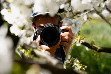 woman taking a photograph using a camera looking at camera with a mirror in the flowery nature....