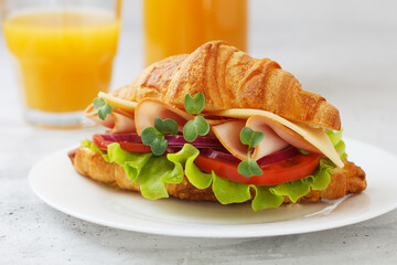 Sandwich with croissant, ham, cheese, tomato, lettuce, microgreens and natural freshly squeezed juice on a gray background