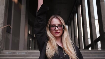 Young attractive woman raising hand with clintched fist up while standing at street. Millennial girl activist supporting movement and fighting for human rights. Concept of protest.