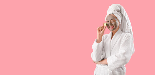 Young woman with applied clay mask and cucumber slice on pink background with space for text