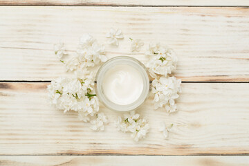 Jar with cream and flowers on color background, top view