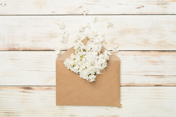Envelop with lilac flowers on wooden background, top view