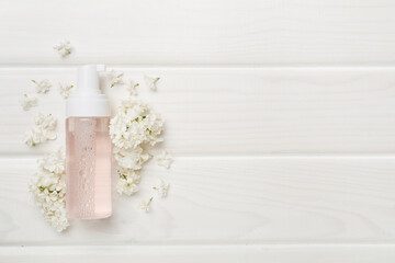 Foaming facial cleanser and with flowers on wooden background, top view