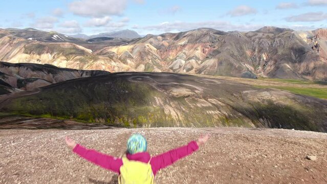 female hiker walking on top of a mountail rising arms aerial view,scenic landscape of landmannalaugar iceland sunny day