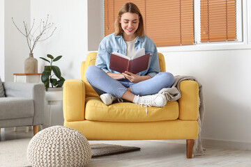 Young woman reading book in yellow armchair at home