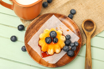 Plate with delicious pudding and blueberries covered by caramel syrup on green wooden background