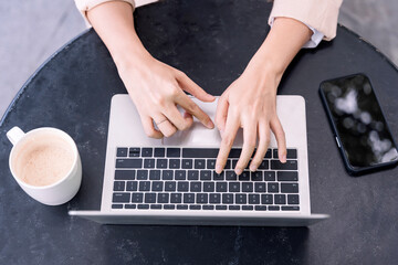 Fototapeta na wymiar Top view of female hands typing on laptop keyboard on black table. Freelance Female hands on the keyboard.