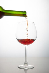 red wine from a bottle is poured into a glass on a light background. alcoholism and addiction. drinks for the holiday