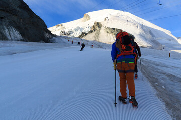 Mountaineer with crampons ascending towards mountain Allalinhorn on ski slope, skiers and snow...