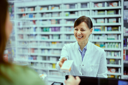A smiling female pharmacist giving a product to a female customer at the drugstore.