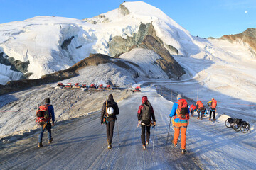 Group of mountaineers with crampons on ski slope ascending towards mountain Allalinhorn and snow...