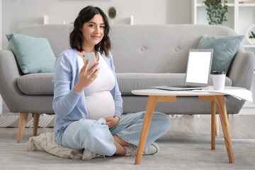 Young pregnant woman working with mobile phone at home