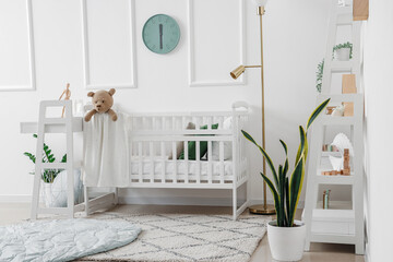 Interior of light bedroom with baby crib, changing table and shelving unit