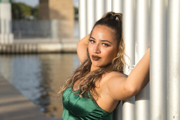 Latin and Hispanic girl, young and beautiful, with green eyes and large eyelashes, with green velvet top, clinging to a fence in a sensual and provocative attitude. Concept beauty, fashion.