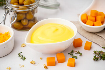 Bowl with tasty cheddar cheese sauce, thyme and olives on white background, closeup