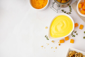Bowl with tasty cheddar cheese sauce, thyme, olives and nuts on white background