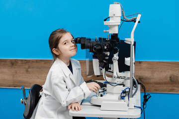 Child doctor ophthalmologist with slit lamp in medical coat. Child is looking through slit lamp. Creative concept of ophthalmology.