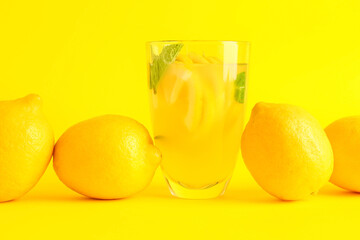 Glass with fresh lemonade and lemons on yellow background