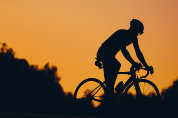 Obraz premium Silhouette of a cycling man riding a bike outside during a sunset