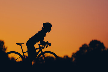 Silhouette of a woman riding a bike during a sport cycling race on a sunset