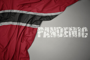 waving colorful national flag of trinidad and tobago on a gray background with broken text pandemic. concept.