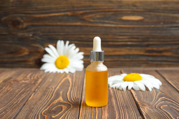 Obraz na płótnie Canvas Bottle of essential oil and fresh chamomile flowers on wooden background