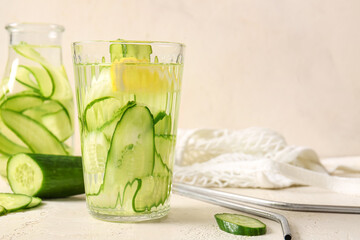 Glass and bottle of infused water with cucumber slices on white table
