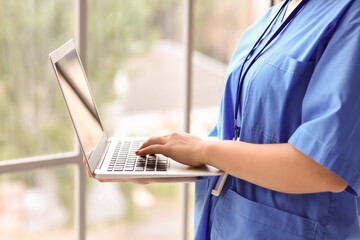 Female medical intern using laptop in clinic, closeup