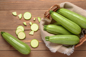 Wicker basket with many fresh green zucchini on wooden background